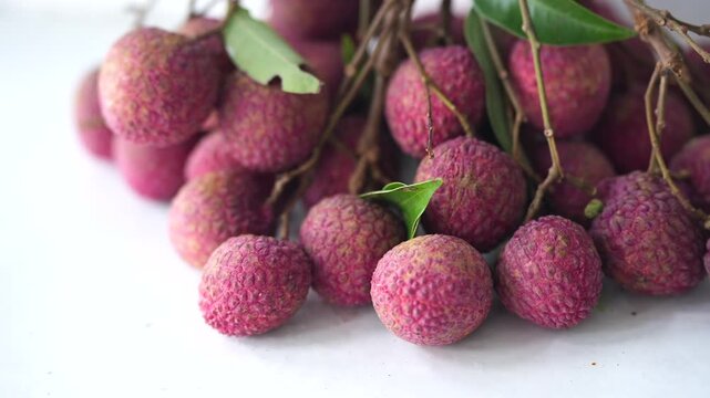 Fresh pink lychees clustered with natural branches and green leaves, showcasing a tropical fruit harvest with vibrant texture.