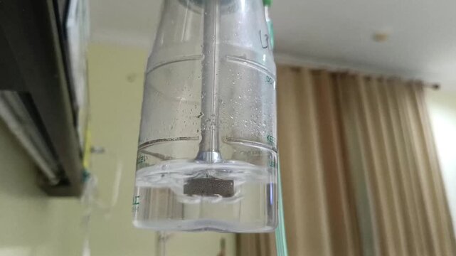 Footage of water bubbles inside a medical oxygen humidifier flowmeter bottle for respiratory therapy in a hospital inpatient room with a soft curtain background.