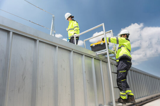 Engineers climbing ladder for industrial rooftop maintenance, Industrial workers carrying tool box for maintenance service on high structure, Team of technicians working on factory building roof