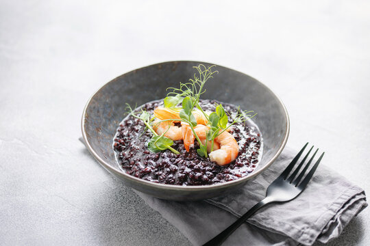 Black rice risotto with shrimps in ceramic bowl. Italian Cuisine.