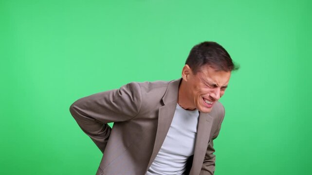 Businessman grimacing in pain from backache on green screen
