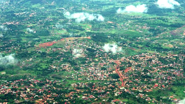 High-angle aerial shot capturing the lush green landscape, scattered houses, and rural villages of Uganda, filmed during a flight near Entebbe.