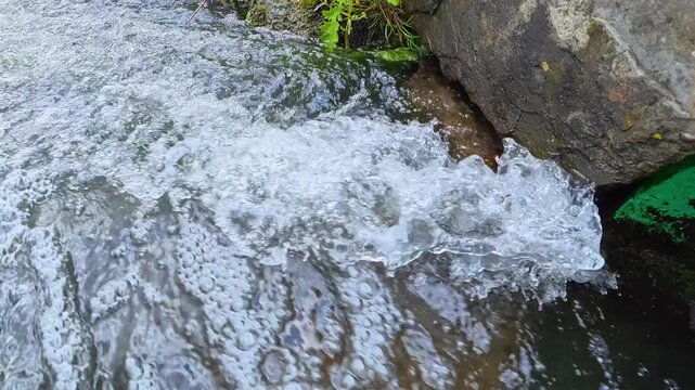 Close-up of clean water flowing from a drainage pipe into a stream with bubbles and splashes