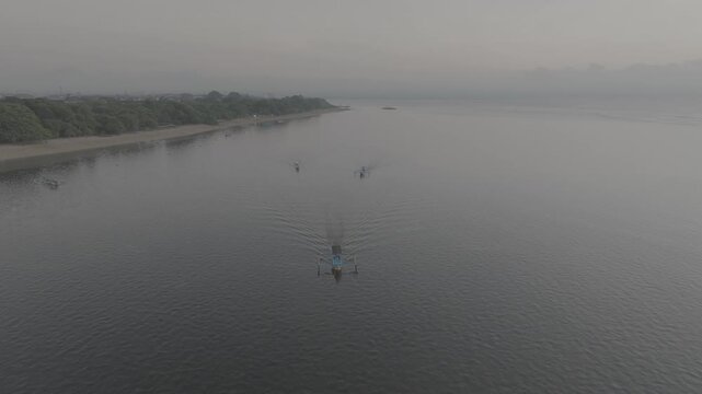 Cinematic aerial drone shot of traditional boat rowing on calm misty lake water during moody morning sunrise, aesthetic foggy nature landscape b-roll.