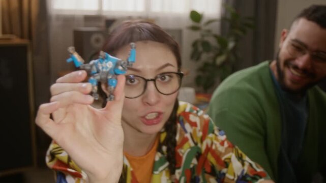 Portrait shot of young adult woman in glasses eating chips and talking to camea while playing mecha tabletop RPG with friends in cozy living room