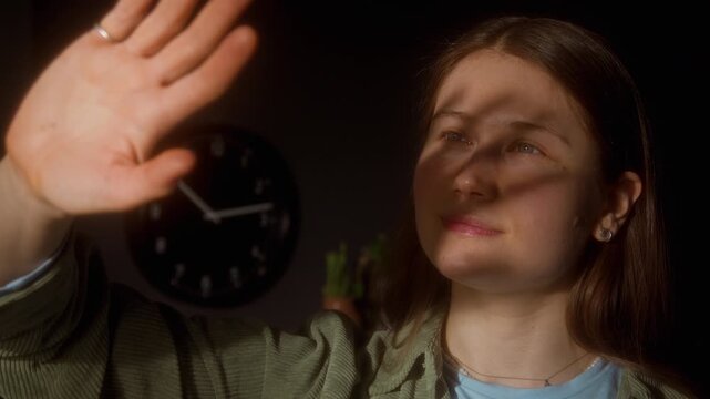 Dreamy shot of smiling young girl waving hand against sunlight rays coming through window and shadow falling on gentle face daydreaming, copy space