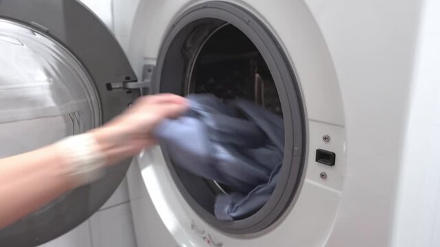 An unknown woman takes colored laundry out of the washing machine. Laundry.