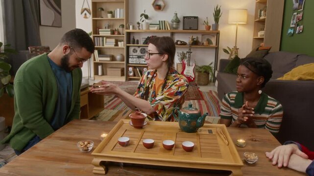 Friends enjoying peaceful tea ceremony with tea set, turquoise teapot, bowls, and candles, passing tea back and forth in cozy living room