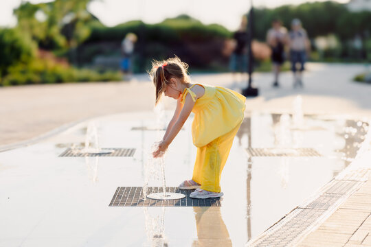 Little girl with fountain water on a sunny summer day. Joyful childhood outdoor moment.