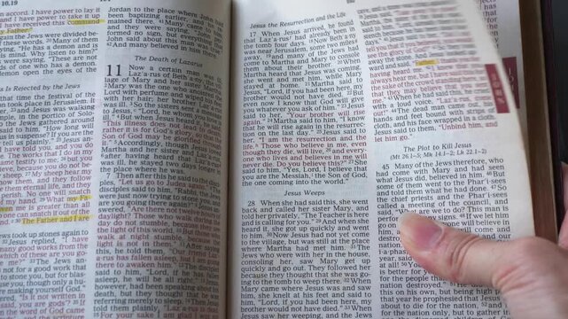 Holy Bible open up to the book of John of the new testament, zooming into Chapter 11 verse 25 on the Jesus as the resurrection and the life. New Revised Stand