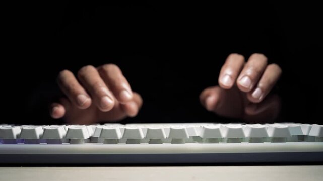 Hands typing on white keyboard in dark low light, Close-up of hands typing on a white computer keyboard in low light with black background