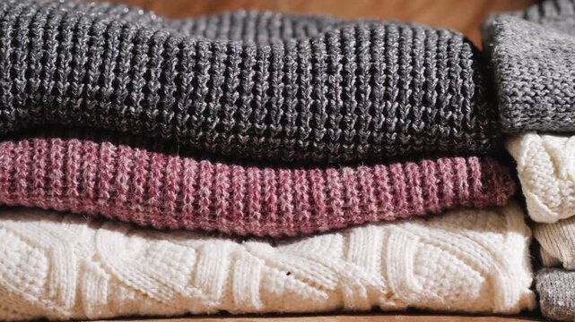 Cozy stacks of folded knit sweaters in warm neutral colors.