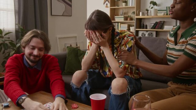 Young woman pretending to be upset when loosing game of poker, having fun with friends in cozy living room