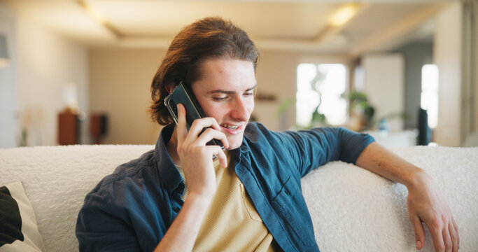 Happy, man and talking with phone call on sofa for friendly discussion, weekend update and relax. Smile, person and mobile chat in living room for social networking, conversation and catch up in home