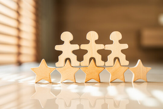 Three wooden human figures standing on five stars rating on a reflective table with sunlight. Concept of excellent teamwork, top customer service, successful leadership, and best human resources.