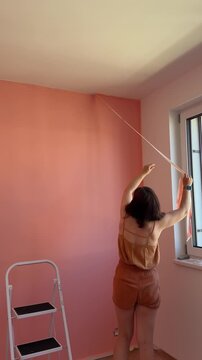 Woman paints walls in room with pink color