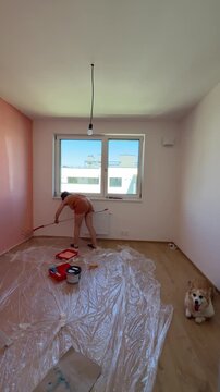 Woman paints walls in room with corgi dog watching