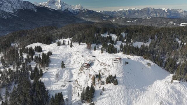 Fly with me across the Bavarian winter landscape at the Mittenwald area with a view to the Alpspitze and Zugspitze complete embedded with snow and ice during a ice cold but blue sky and sunny day