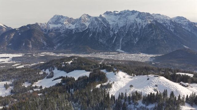 Fly with me across the Bavarian winter landscape at the Mittenwald area with a view to the Alpspitze and Zugspitze complete embedded with snow and ice during a ice cold but blue sky and sunny day