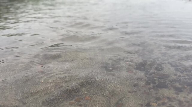 Close up of clear water flowing gently over a dark sandy riverbed