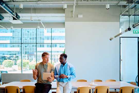 Two diverse business partners discussing work, collaborating and planning in a modern meeting room with a digital tablet