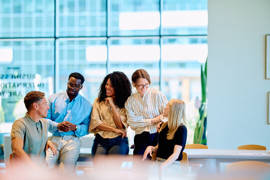 Diverse business professionals smiling and talking during an informal meeting, reflecting teamwork, collaboration, and modern workplace communication