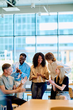 Multiracial young professionals meeting in a modern office, applauding and smiling, showing teamwork, support, and achievement