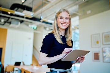 Young business woman smiling, using a digital tablet for work in a modern office environment....