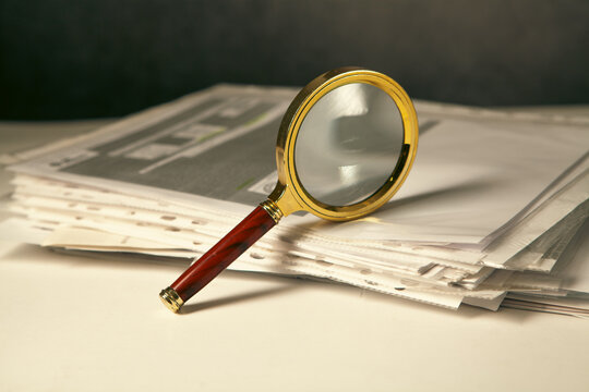 A magnifying glass on top of a pile of newspapers. Selective focus.