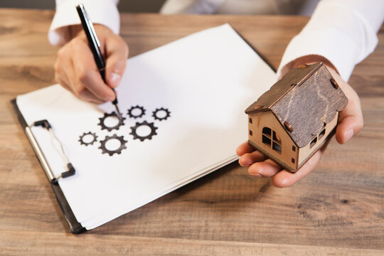 Close-up of woman holding model of house and writing in notebook