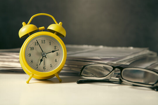 Yellow alarm clock and eyeglasses on the table. Time management concept