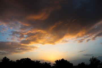 Fototapeta premium Dramatic cloudscape during sunset with glowing horizon light. Nature landscape capturing an intense sunset with richly detailed clouds and warm sunlight fading into the horizon. 