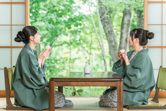 A woman and her friend drinking sake in yukata in a Japanese-style room at a traditional Japanese inn.