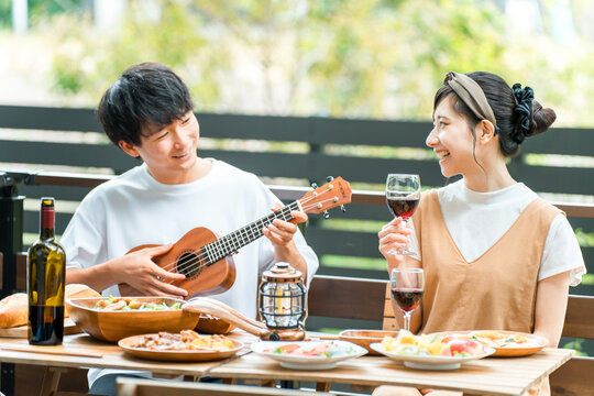 Young Asian men and women, couples enjoying a barbecue, home party, and glamping on a wooden deck.