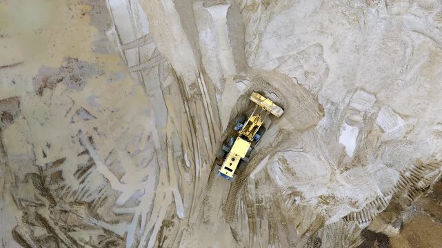 Aerial view shows yellow mining truck on sandy terrain. The truck moves through a large excavation site. Dusty landscape emphasizes industrial scale. Ideal for construction or mining projects