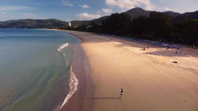 Aerial phuket beach lone runner is sprinting along shoreline during sunrise near turquoise water on smooth sand. Peaceful atmosphere and fitness focus with the travel inspiration filmed by drone