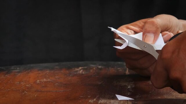 A man's hand cuts a sheet of white paper with scissors and cuts off the corners. Close-up, DIY concept.