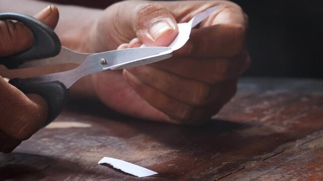 A man's hand cuts a sheet of white paper with scissors and cuts off the corners. Close-up, DIY concept.