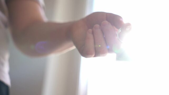 A woman's hand holds a keychain With a key and a keychain in the shape of a house. Soft light in the room from the window. The concept of purchasing a house.