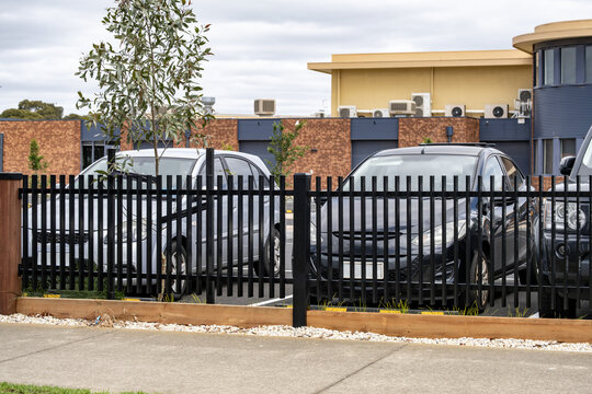A modern black steel palisade security fence lines the boundary of a suburban commercial property or a car parkin Australia. Powder-coated tubular steel fencing with decorative garden edging
