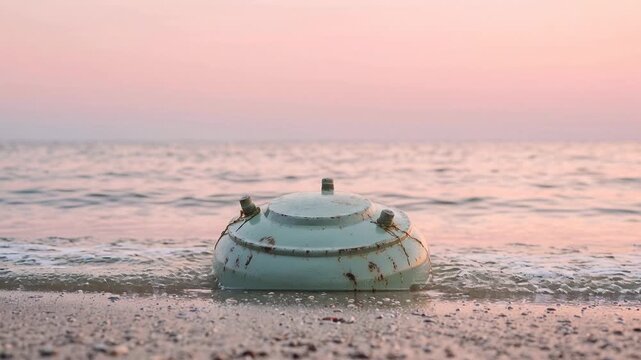 Old sea mine washes ashore on a tranquil beach at sunset
