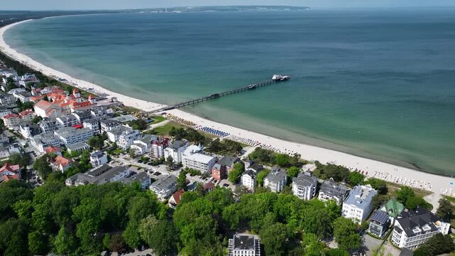Aerial footage of Binz seaside resort on island of R&uuml;gen, Germany with long pier extending into Baltic Sea, sandy beaches, spa architecture, coastal promenade, and excursion boat.