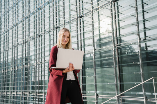 Blond businesswoman with laptop in the background of modern office building