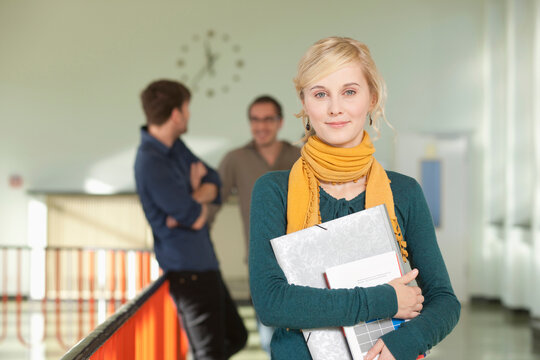 Germany, Leipzig, Young woman holding book with students standing in background