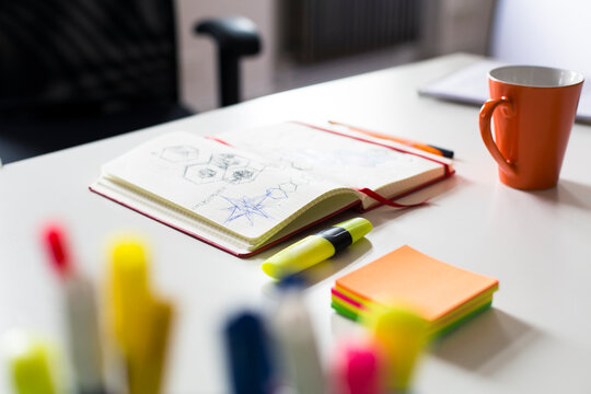 Notebook with sketch, highlighters and cup of coffee on desk in office