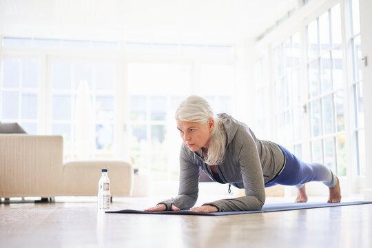 Retired active senior woman practicing plank position on mat at home