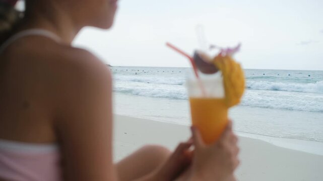 Teenage girl in profile sipping a fresh mango smoothie through a straw on a sunny beach, selective focus. Summer refreshment concept