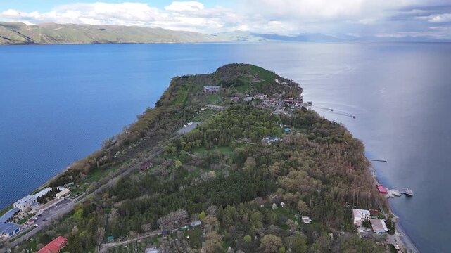 Aerial drone view of narrow peninsula with two small boats surrounded by blue lake water under dramatic cloudy sky 4K.