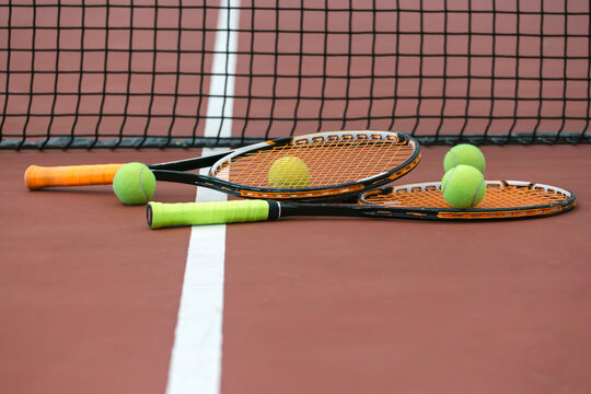 Two tennis rackets and four balls lying on ground of tennis court
