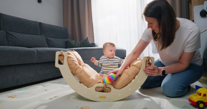 Mother playing and interacting with her baby on the floor in a cozy living room, encouraging development and bonding with wooden toys and colorful rattle